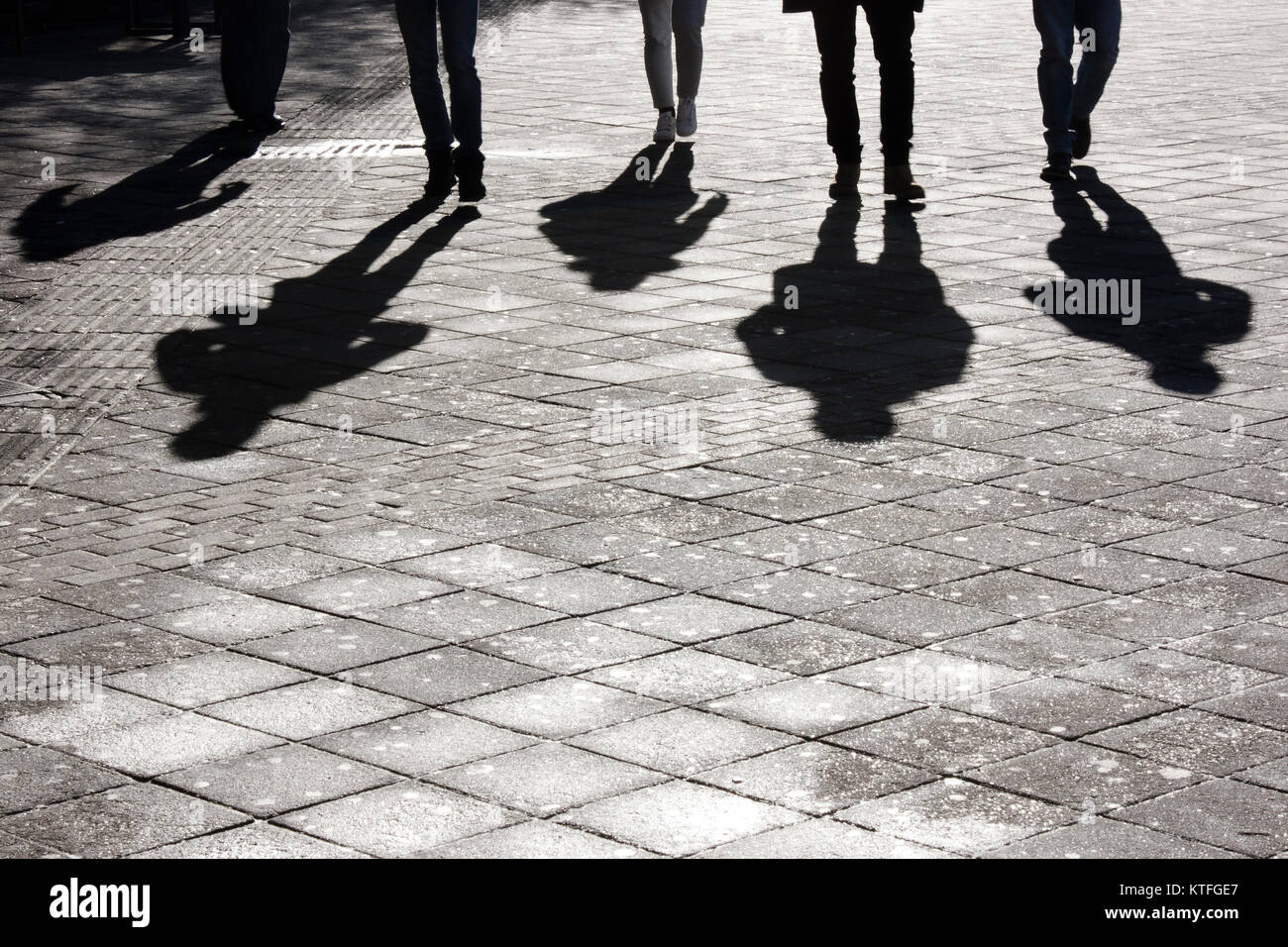 Legs and shadow of five young person approaching on city street