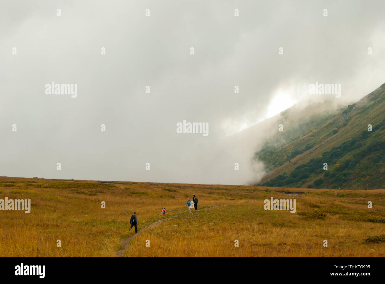 RUSSIA, KRASNODAR KRAI - SEPTEMBER 23, 2017: tourists walk on a mountain plateau in Caucasus Nature Reserve, admiring the cloud rising from behind the Stock Photo