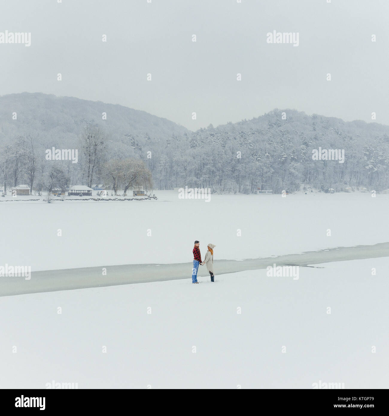 Loving couple is holding hands near the frozen river on the snowy ...