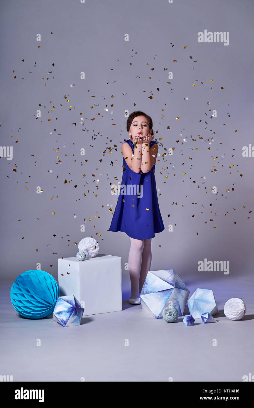 Cute baby girl in blue dress pretty model enjoying holiday and throwing confetti.Minimalism and origami. Stock Photo