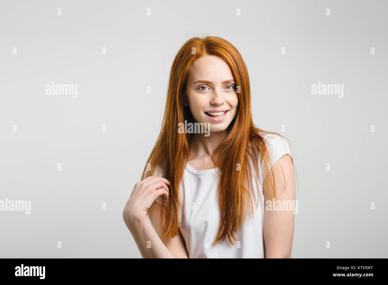 girl smiling with closed eyes touching her red hair over white background Stock Photo