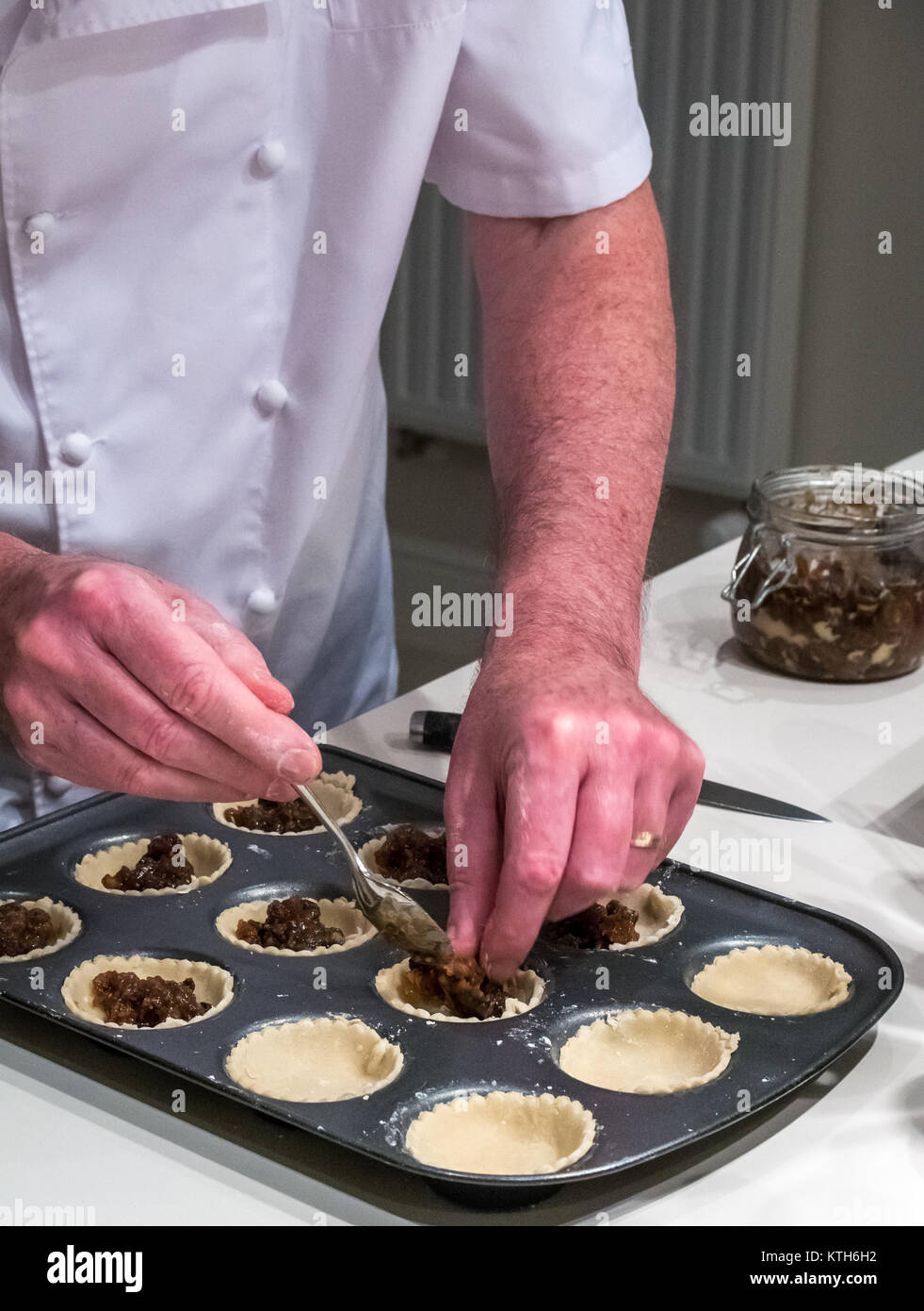 Older man in chef whites filling mince pie cases ready for baking at Christmas time in a kitchen Stock Photo