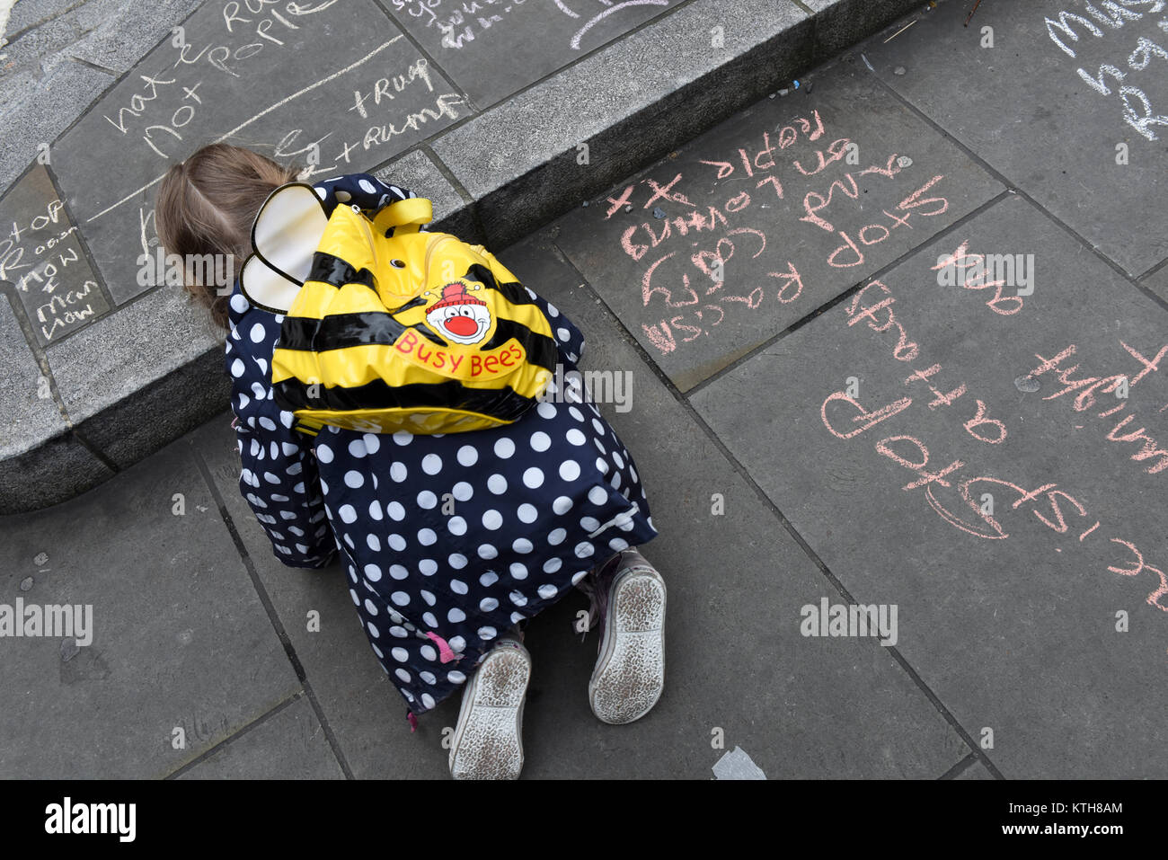A child protester is writing anti-Trump and anti-racism messages on the pavement during the UN Anti-Racism Day in London, UK. Stock Photo
