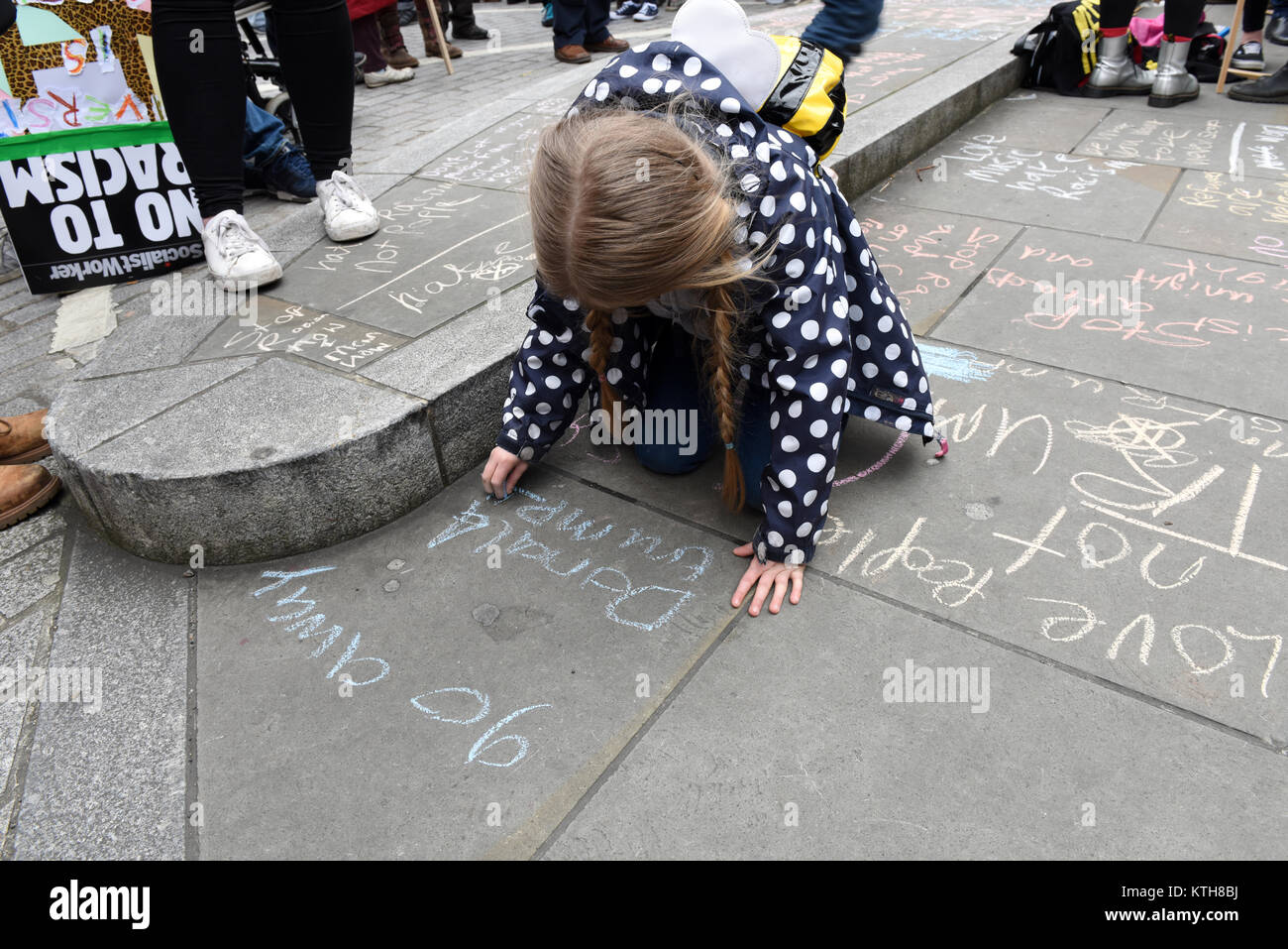A child protester is writing anti-Trump anti-racism message reading: 'go away Donald Trump' on the pavement during the UN Anti-Racism Day in London, UK Stock Photo