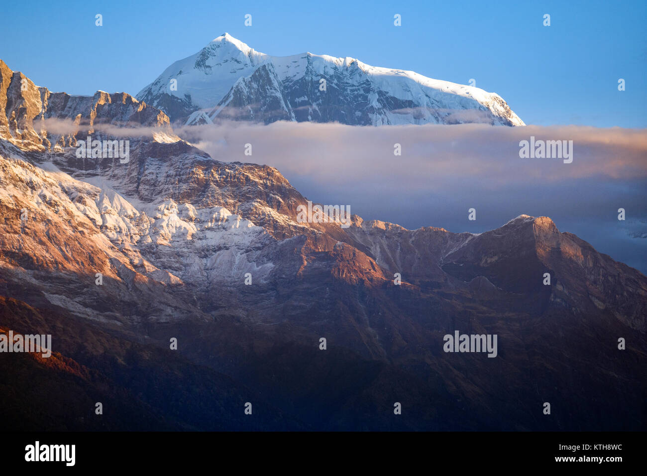 Edge of the Annapurna mountain range rises above the clouds and behind the slope of Fishtail mountain. Stock Photo
