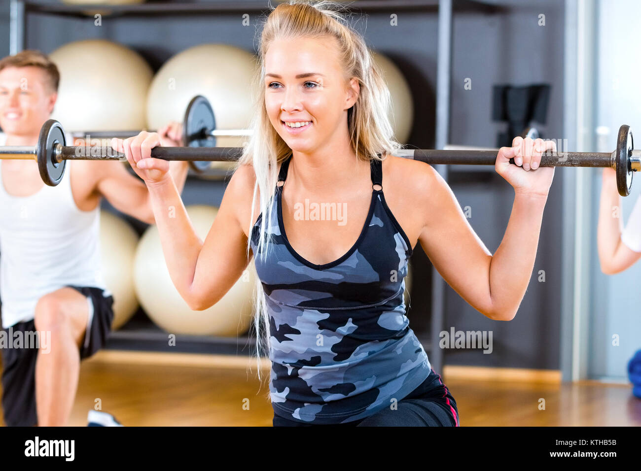 Close-up of Young Woman Lifting Barbell Rod With Friends In Gym Stock Photo