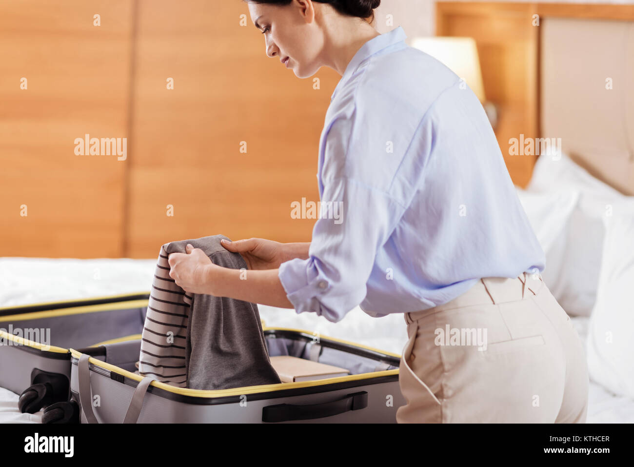 Earnest focused woman taking her clothes from luggage Stock Photo