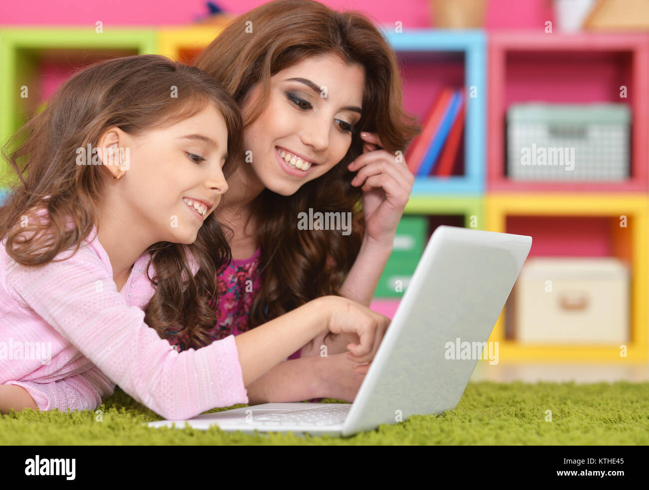Beautiful young woman and little girl lying on floor and using laptop ...