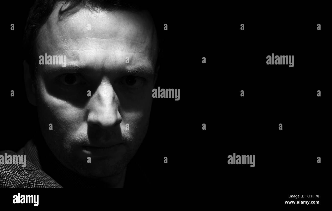 Closeup studio portrait of young adult man over black background low key black and white photo