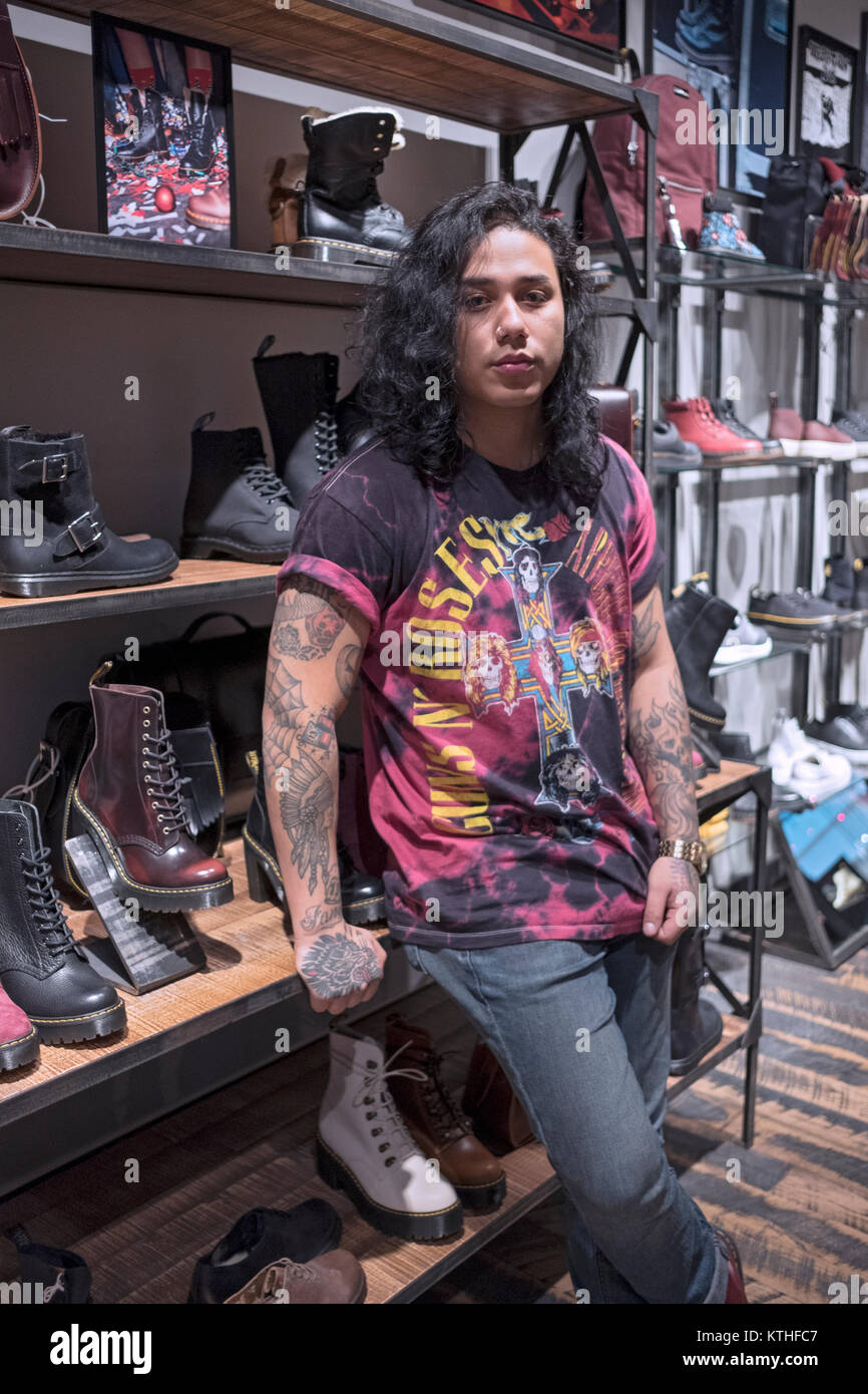 A young male salesman with long hair at the Dr. Martens store at the Queens Center shopping mall in Elmhurst, Queens, New York City. Stock Photo