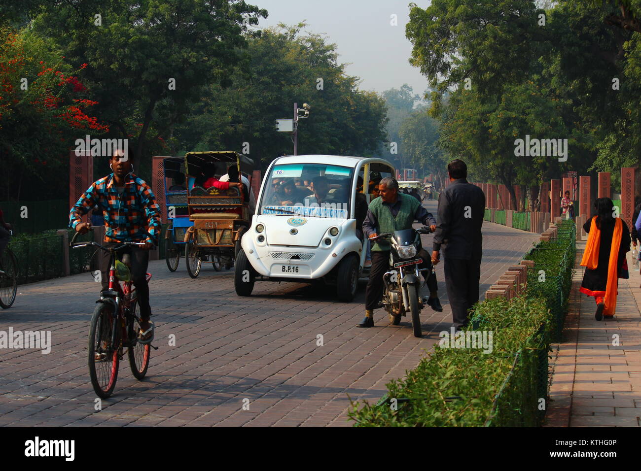 A cyclist wearing earphones moving in front of an Electric van ferrying tourists from Taj Mahal Eastern Gate to Shilpgram in Agra, Uttar Pradesh. Stock Photo