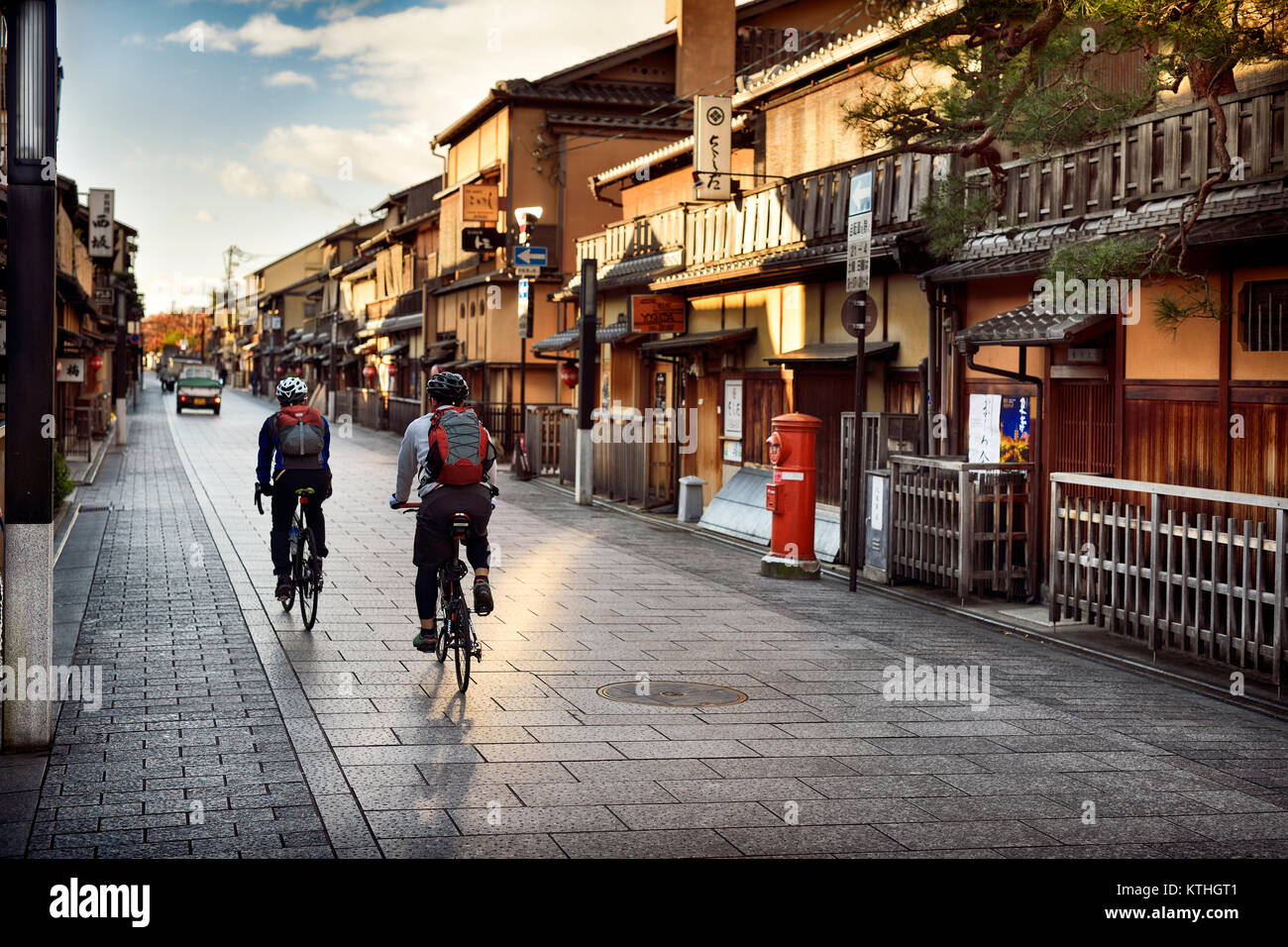 Cyclists on an empty Hanamikoji Dori street in Gion district in morning sunrise before all the shops and restaurants start opening. Hanami-koji, Gionm Stock Photo