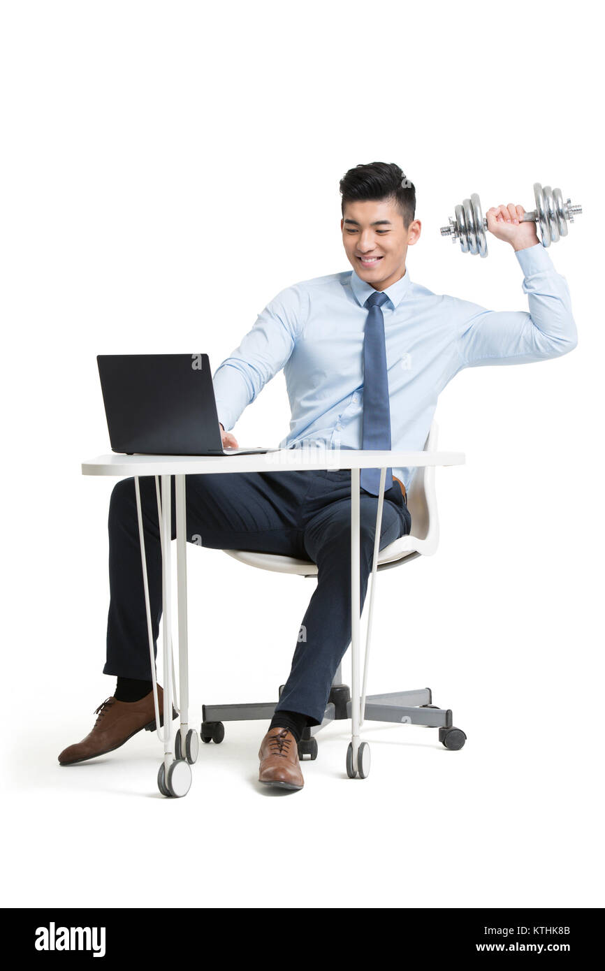 Young businessman lifting weights while using laptop at work Stock ...