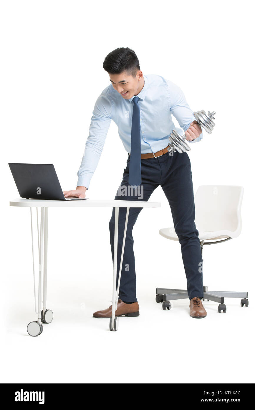 Young businessman lifting weights while using laptop at work Stock ...