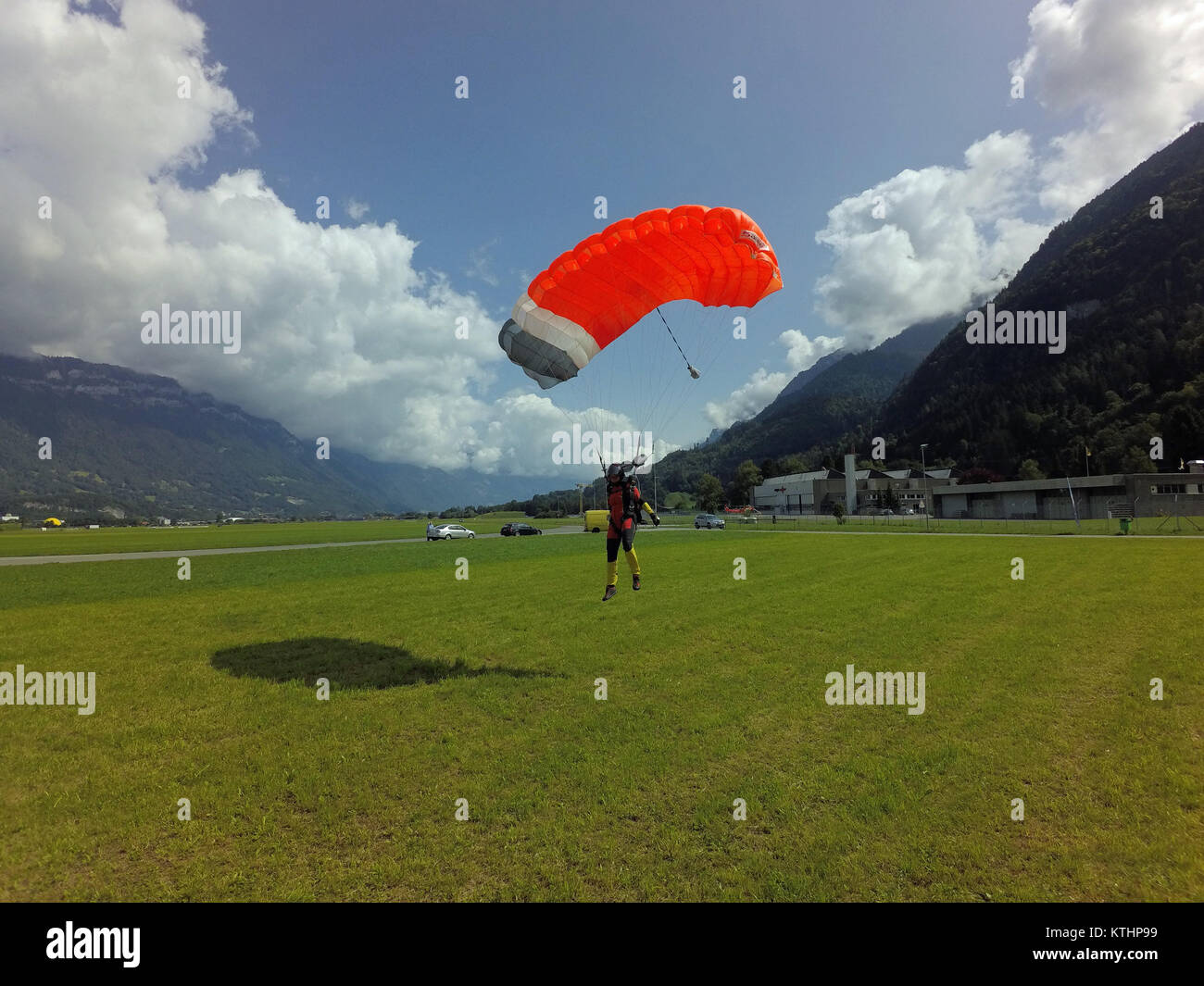 Parachuter under canopy is landing save on the dedicated grass area. She has a big smile on her face after this skydive jump. Stock Photo