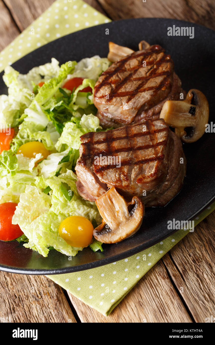 fillet mignon steak with vegetable salad and mushrooms close-up on a plate on a table. vertical Stock Photo
