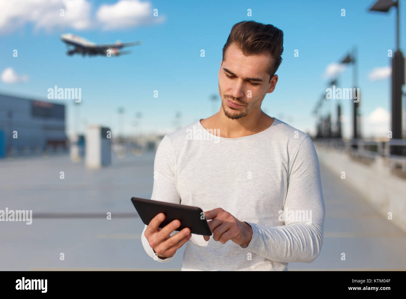 Young caucasian man booking flight ticket by tablet outdoors on airport Stock Photo