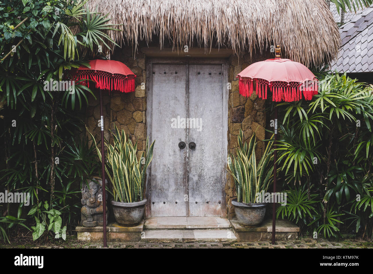 Entrance in traditional bali house with wooden door, straw roof and red umbrellas Stock Photo