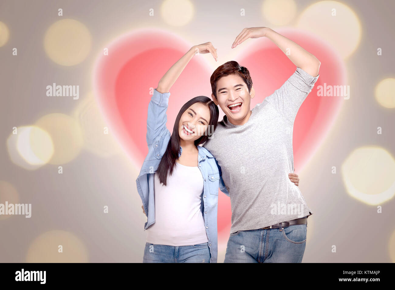 Romantic asian couple in love make heart with hand over blur light ...