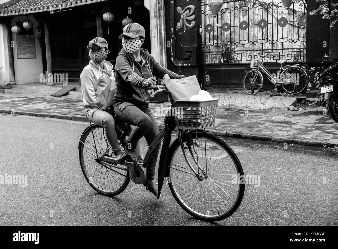masked cyclist and passanger riding though thr streets of Hoi An Ancient Town, Vietnam. Stock Photo