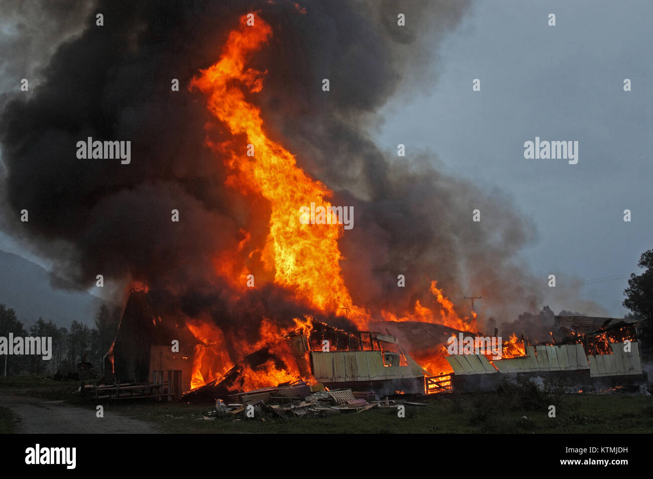 flames and smoke rise from burning farm building Stock Photo