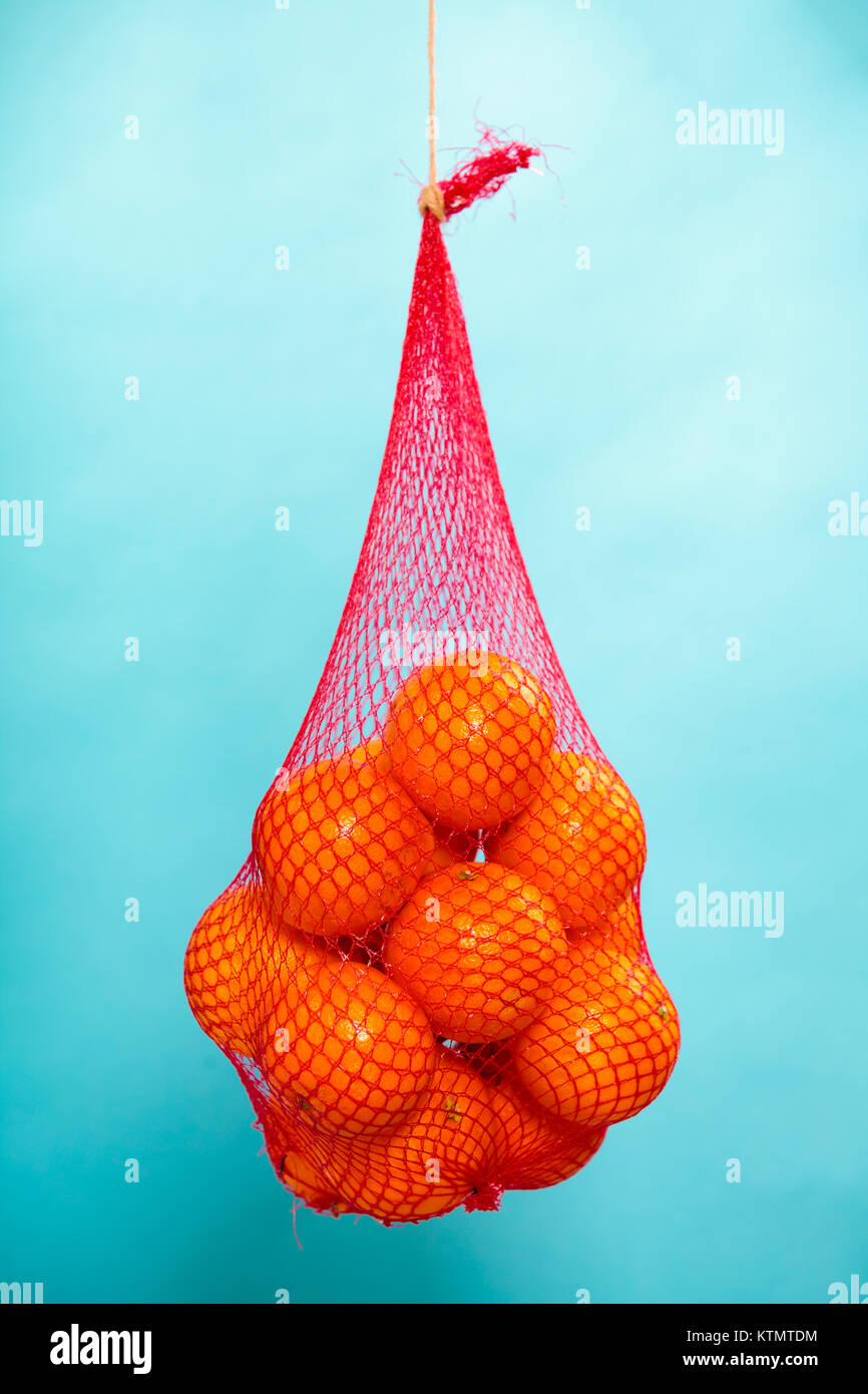 Mesh bag of fresh oranges healthy tropical fruits from supermarket on blue. Food retail. Stock Photo
