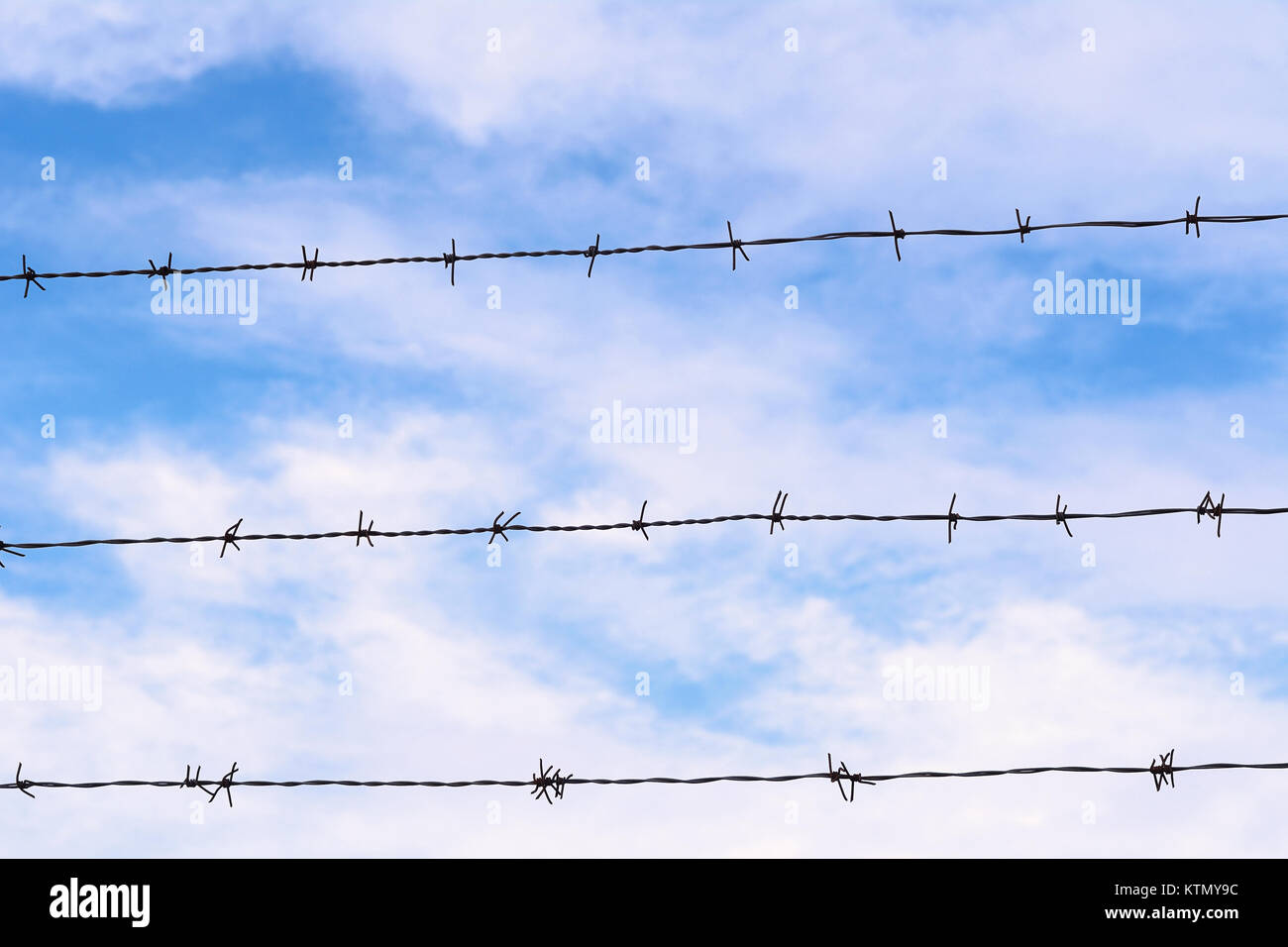 Fence of barbed wire against blue sky with clouds Stock Photo - Alamy