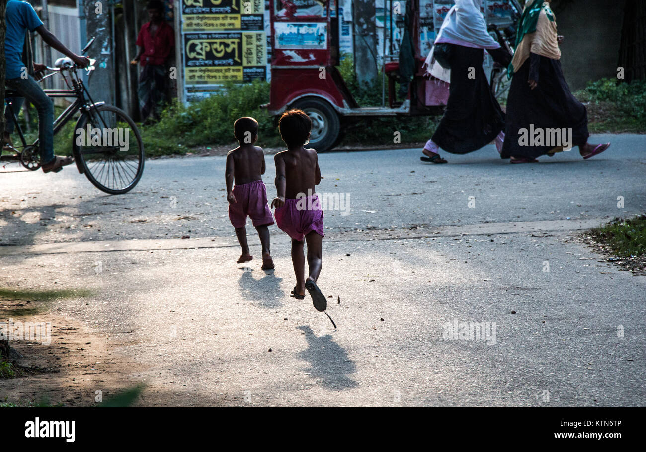 Two kids and two women in veils walk past a city street. of Khulna Stock Photo