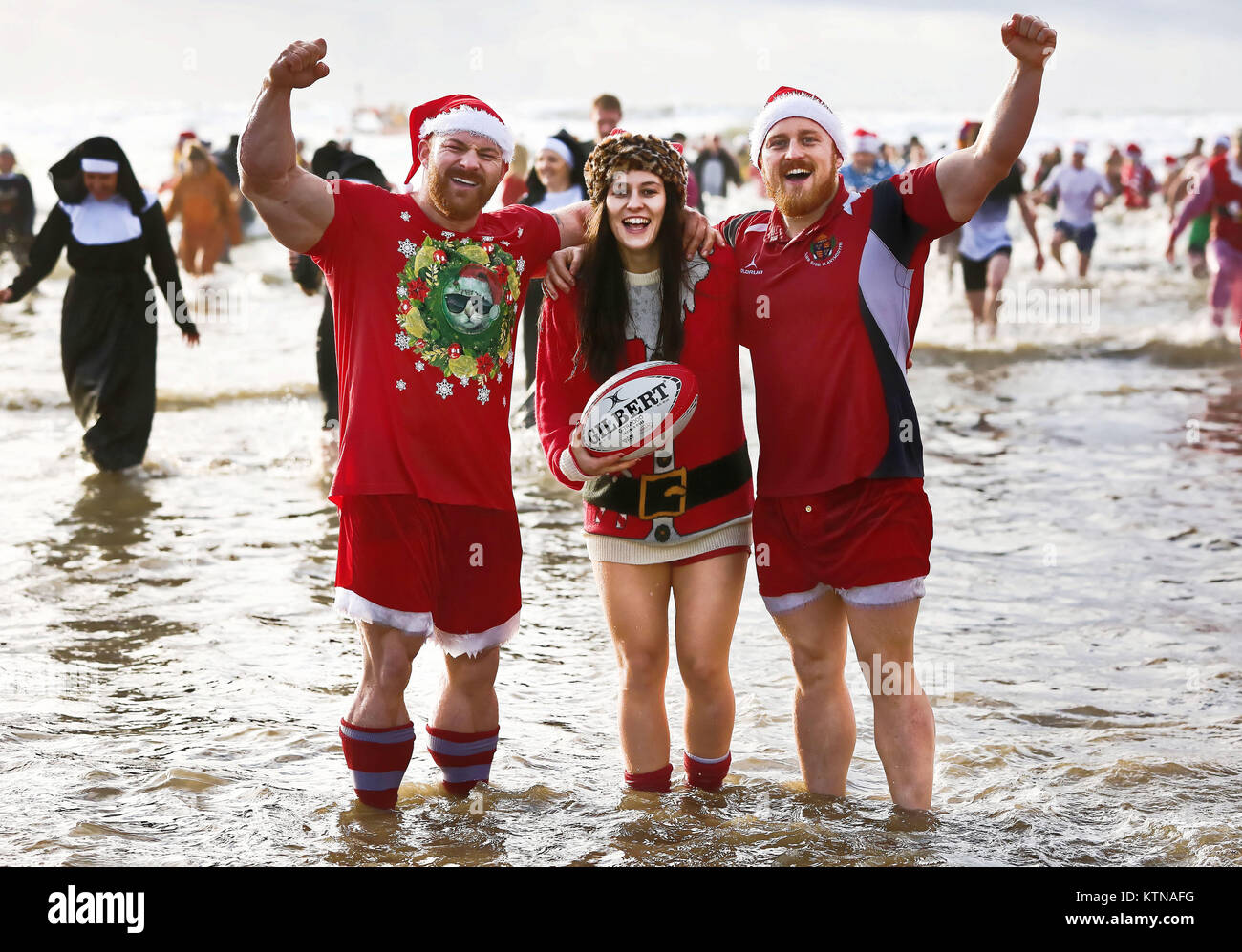 Three people wearing a combination of Santa and rugby outfits take to the water Stock Photo