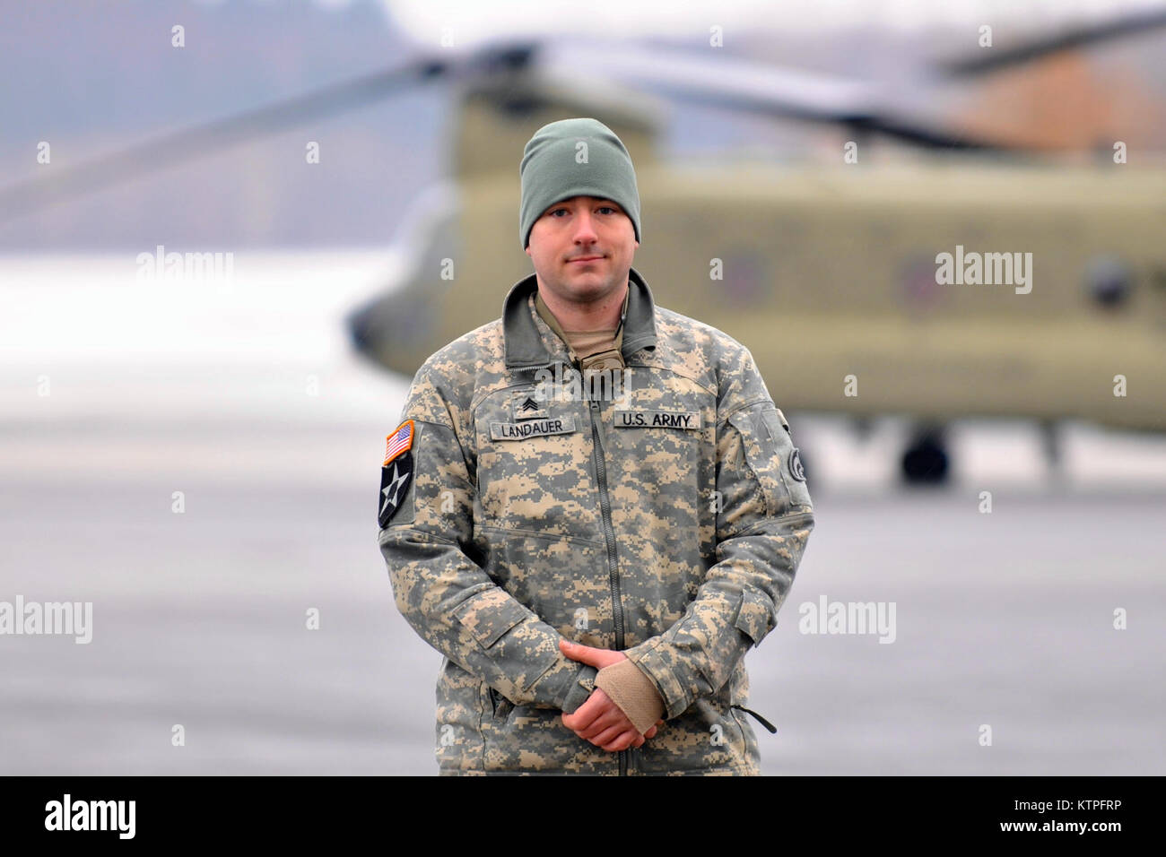 SYRACUSE, NY - Army Staff Sgt. Mike Landaur stands in front of a CH-47F Chinook Helicopter at Hancock Field Air National Guard Base on March 14, 2015. Staff Sgt. Landaur is a CH-47F crew chief from Company B, 3rd Battalion, 126th Aviation based at the Army Aviation Support Facility at Rochester International Airport. 30 Airmen from the 274th Air Support Operations Squadron (ASOS), based at Hancock Field and the Army aircrew trained together for the first time. The training included Joint Terminal Attack Controller (or JTAC) Airmen from the 274th ASOS conducting CH-47 helicopter familiarization Stock Photo