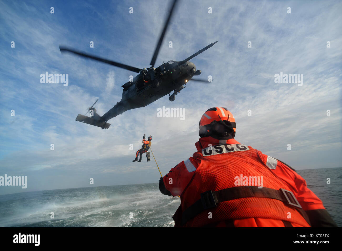 HAMPTON BAYS, NY -  Machinery Technician 2nd Class Benjamin Esposita helps wrangle a hoist line from an HH-60 Pavehawk from the 101st Rescue Squadron during training in the waters near US Coast Guard Station Shinnecock December 22, 2016.  During this training, Guardian Angels from the 103rd RQS were lowered via hoist from an HH-60 Pavehawk onto the cutter's deck. After that, the aircraft practiced dropping and removing patient litters, before hoisting the Guardian Angels back up and returning to base.  (US Air National Guard / Staff Sergeant Christopher S. Muncy / released) Stock Photo