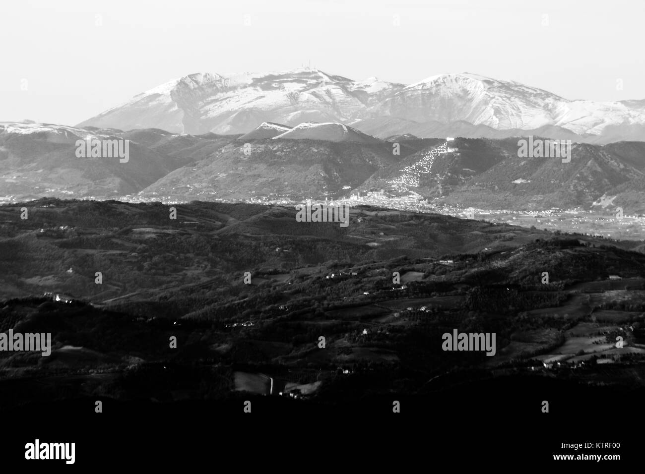 Umbria valley in winter, with a view of Gubbio town with big, lighted Christmas tree on the mountain side and Monte Cucco covered by snow Stock Photo