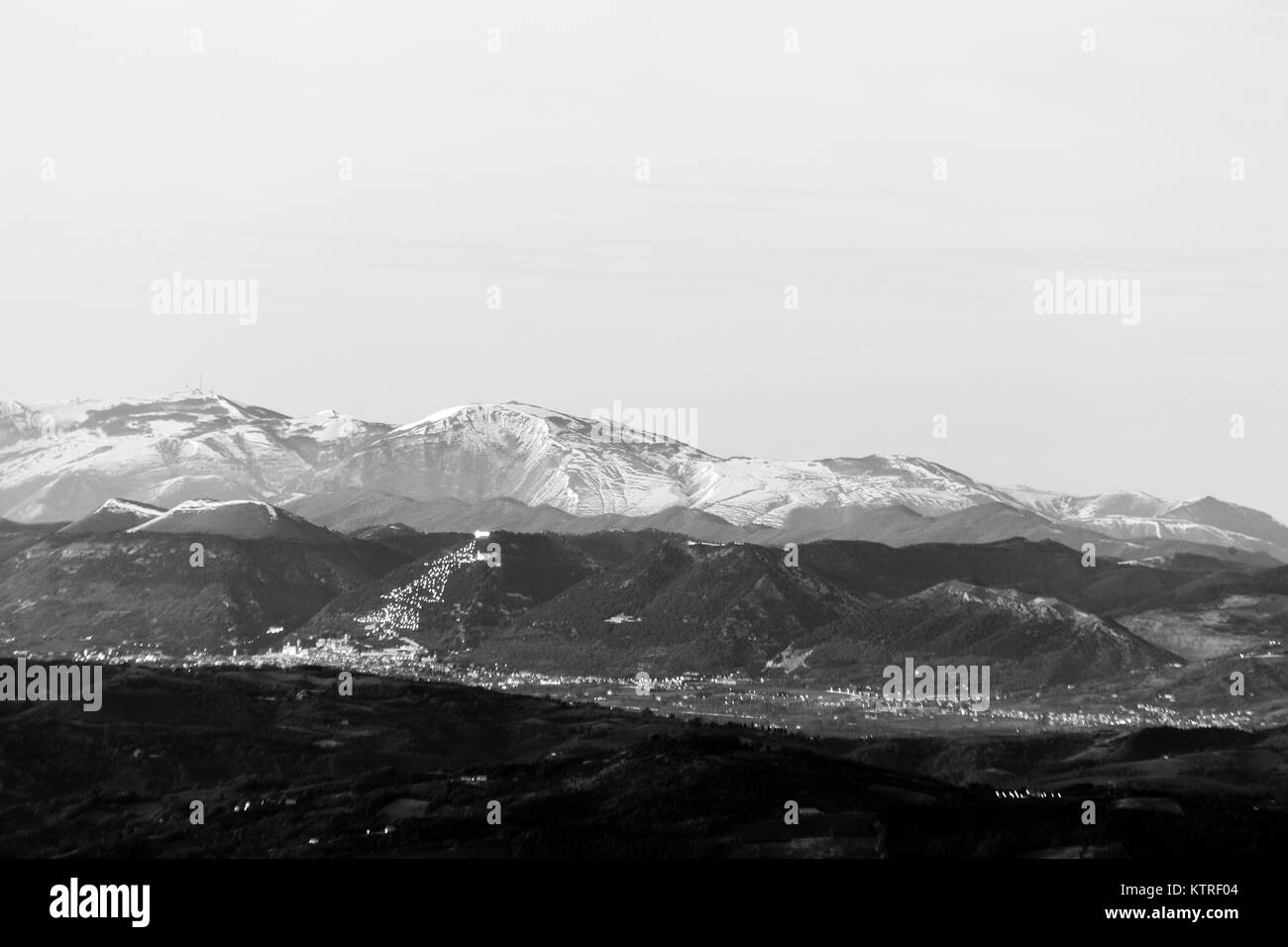 Umbria valley in winter, with a view of Gubbio town with big, lighted Christmas tree on the mountain side and Monte Cucco covered by snow Stock Photo