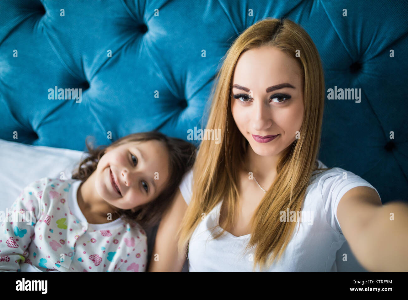 Mother and daughter lying on bed and taking self portrait with