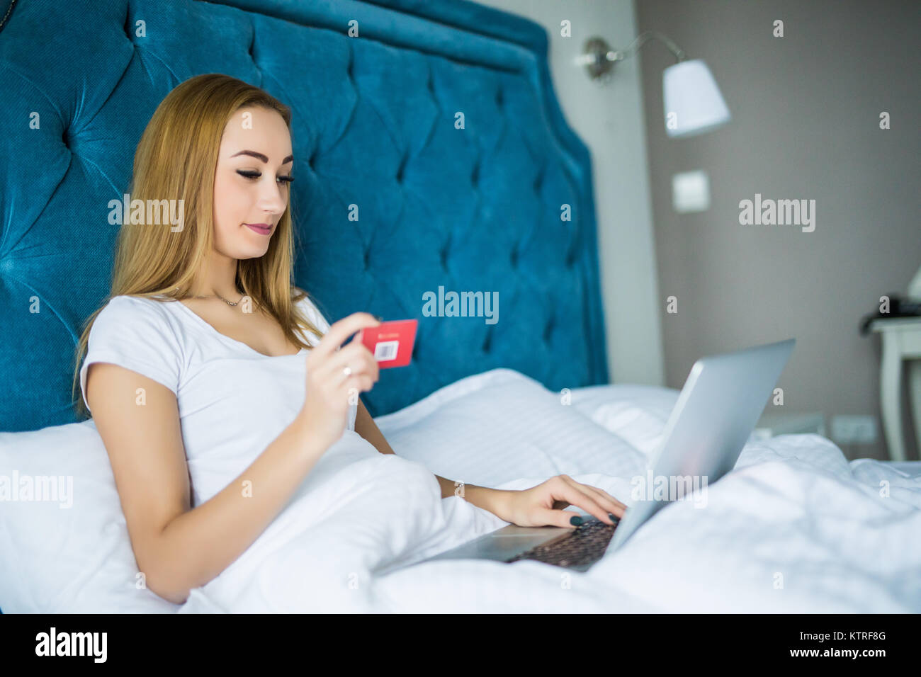 A smiling woman lying on her bed with her credit card in hand as she ...