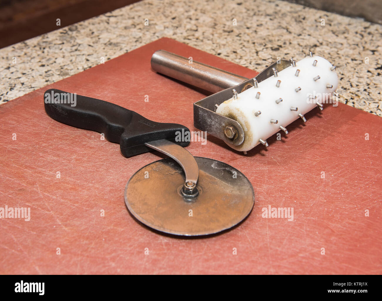 Pizza base roller and wheel cutter laying on chopping board at fast food snack bar Stock Photo