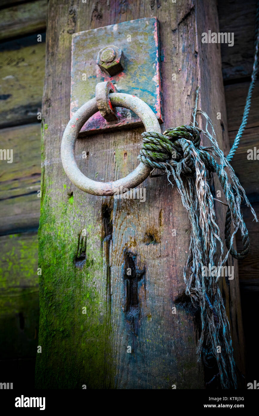 Cast iron mooring ring with frayed nylon rope on a wooden pier Stock Photo