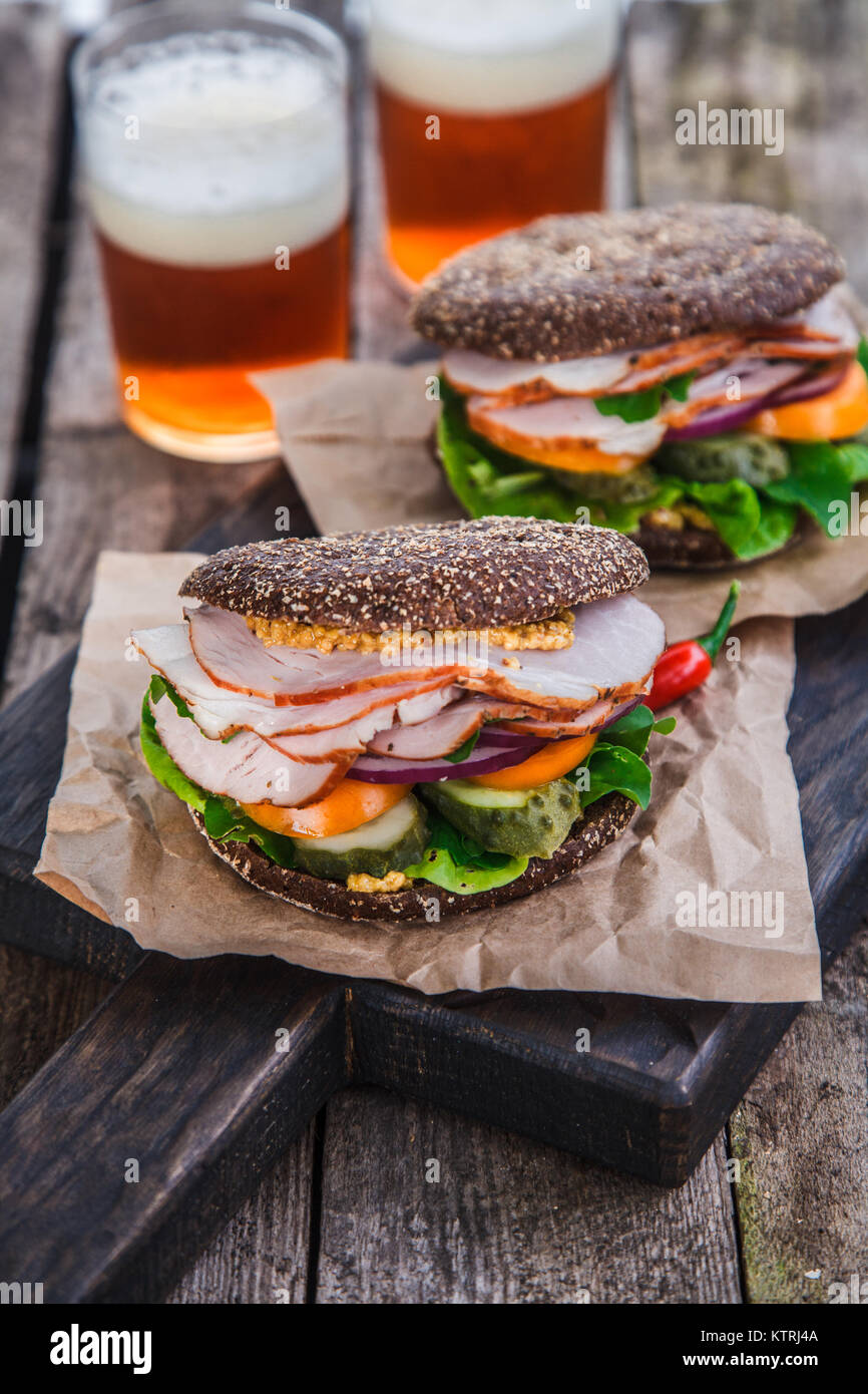 rye sandwiches with ham and letucce on wood table with two glasses of ...