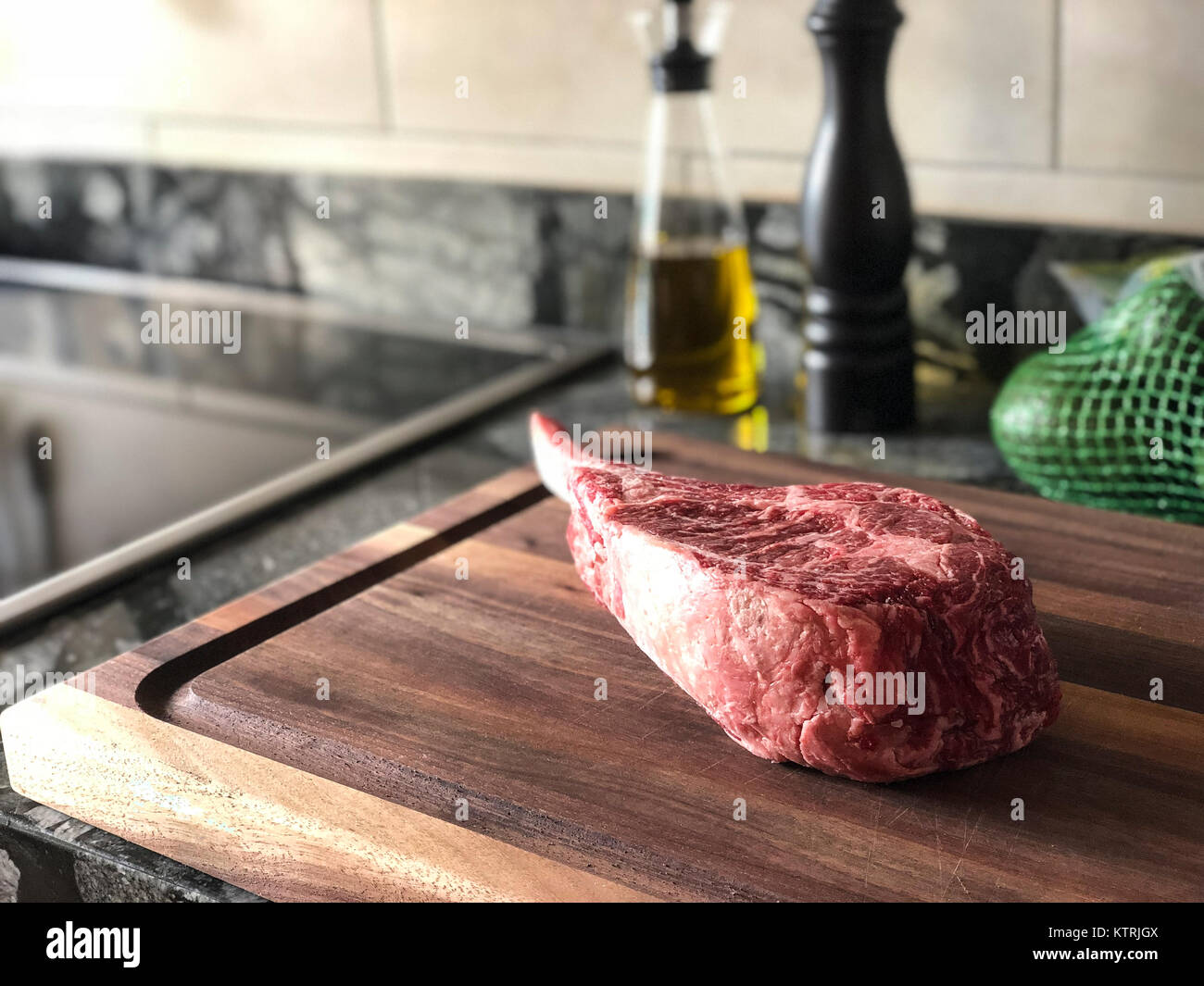 Horizontal close up photo of bone-in ribeye steak with oil dispenser and pepper mill in the background on a kitchen counter. Stock Photo
