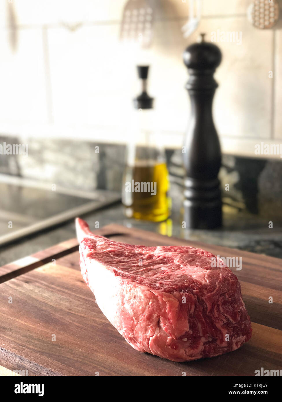 Close up of raw thick tomahawk ribeye beef steak on cutting board. Oil dispenser and pepper mill in the background. Stock Photo