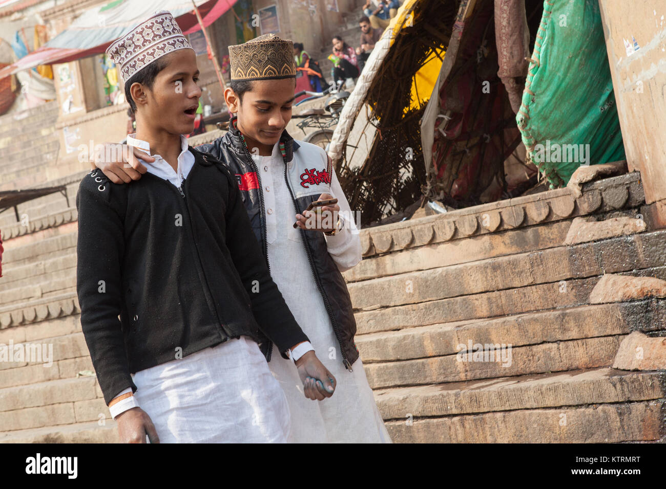 A teenager looks at his smartphone as he walks with his friend on the ghats at Varanasi Stock Photo