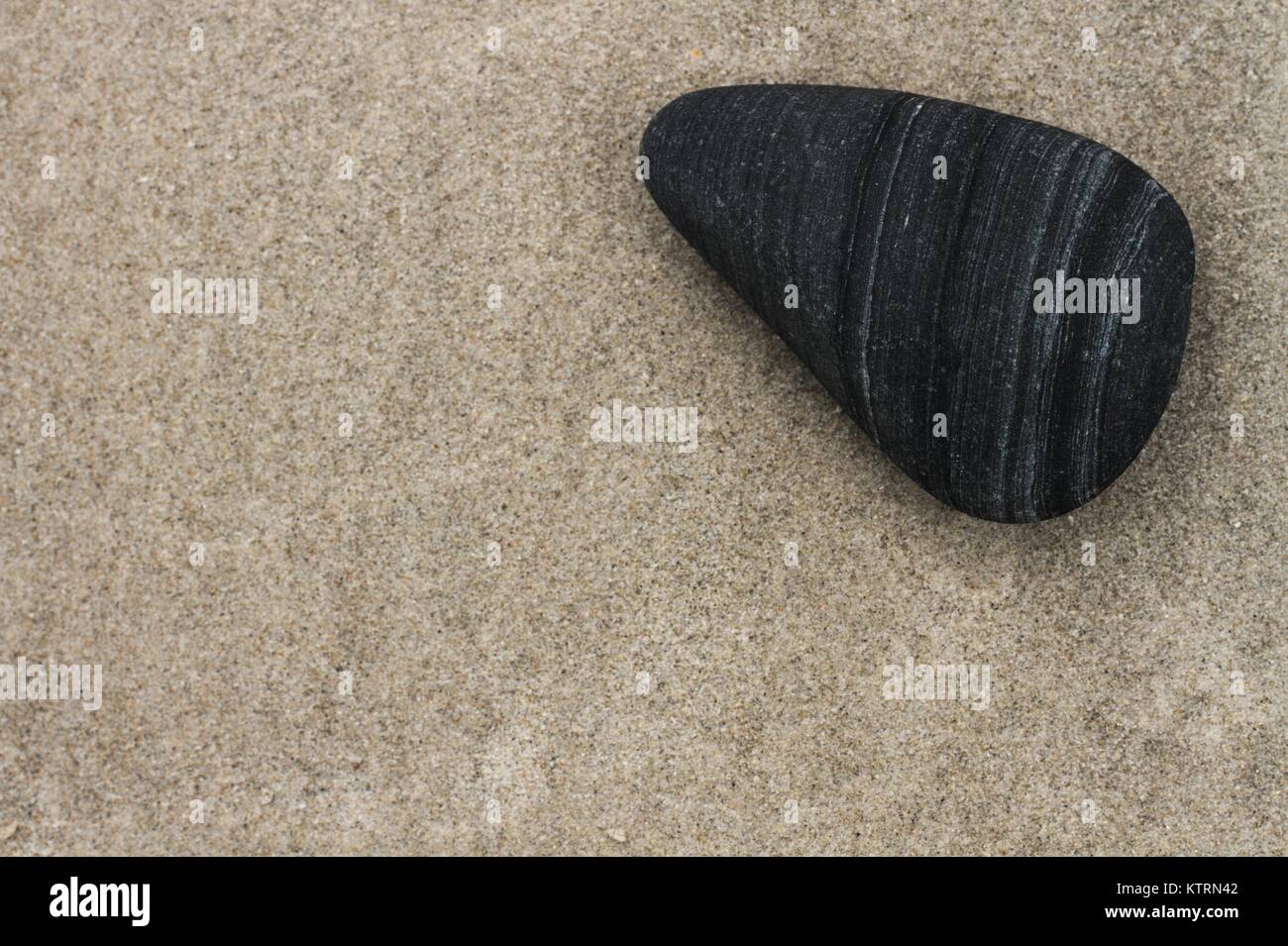 Smooth triangular black stone against sandy background. Stock Photo