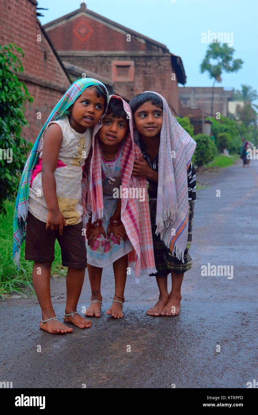 Kids standing and protecting themselves with a towel from rain Stock Photo