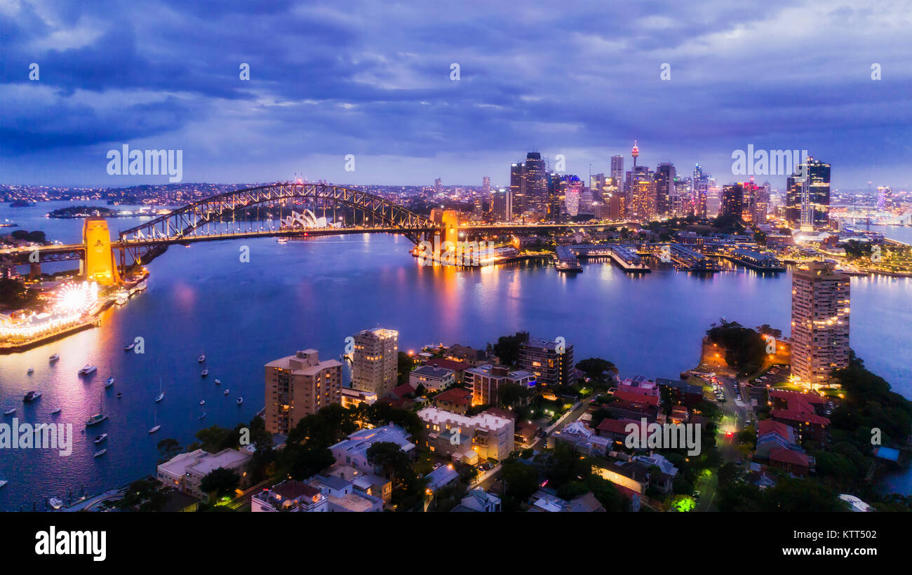 Sydney city CBD from Blues Point and North Sydney at sunset with bright illiumination of famours landmarks around Harbour in elevated aerial shot. Stock Photo
