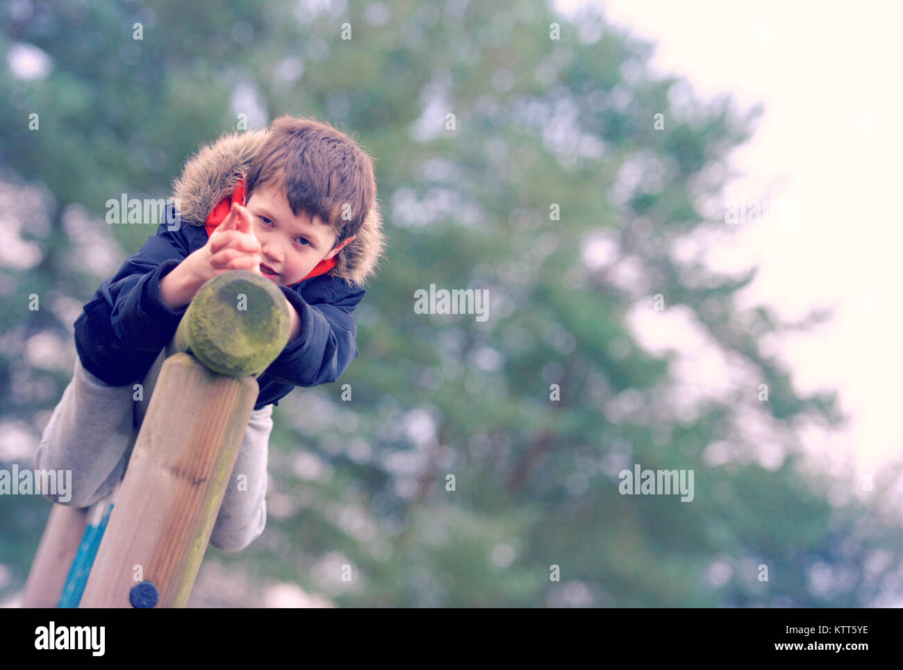 Boy on a climbing frame pretending to shoot a gun Stock Photo