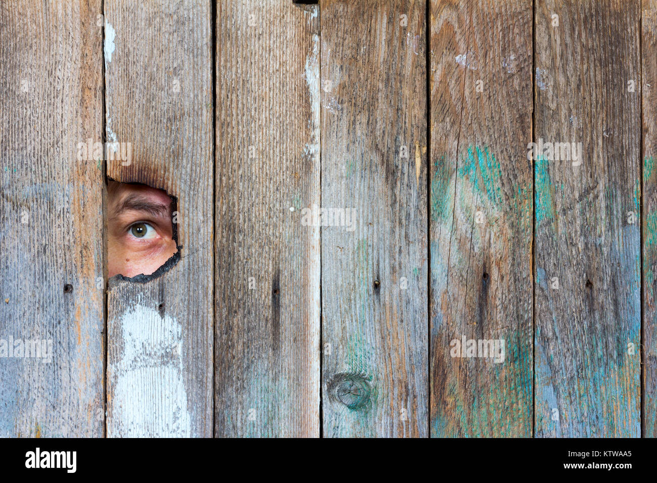 the eyes of a man spying through a hole in an old wooden fence. with space for posting information Stock Photo