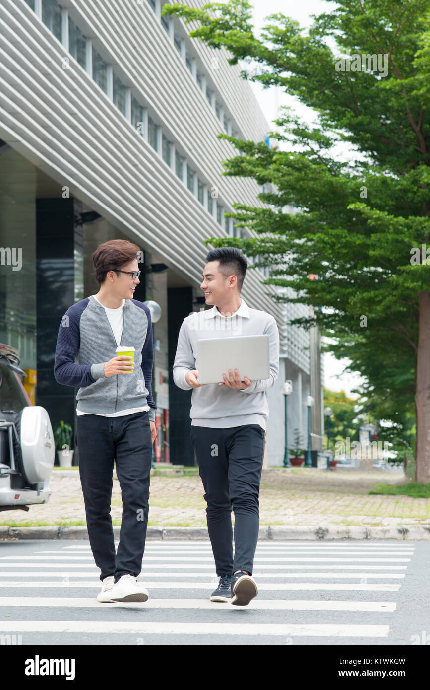 Two smiling young businessmen walking and talking in the city Stock ...