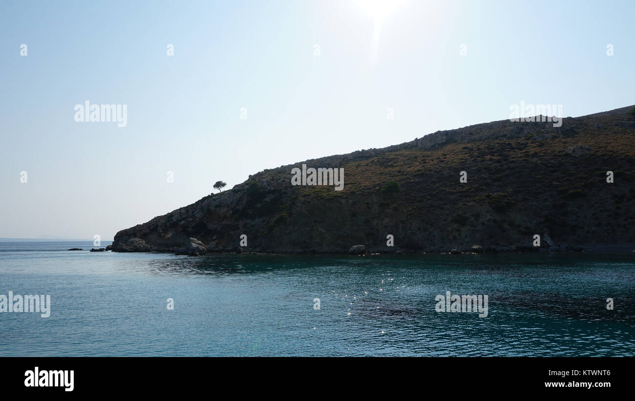 The edge of a Greek island, rich blue sea with a tree on the top of a cliff. Stock Photo