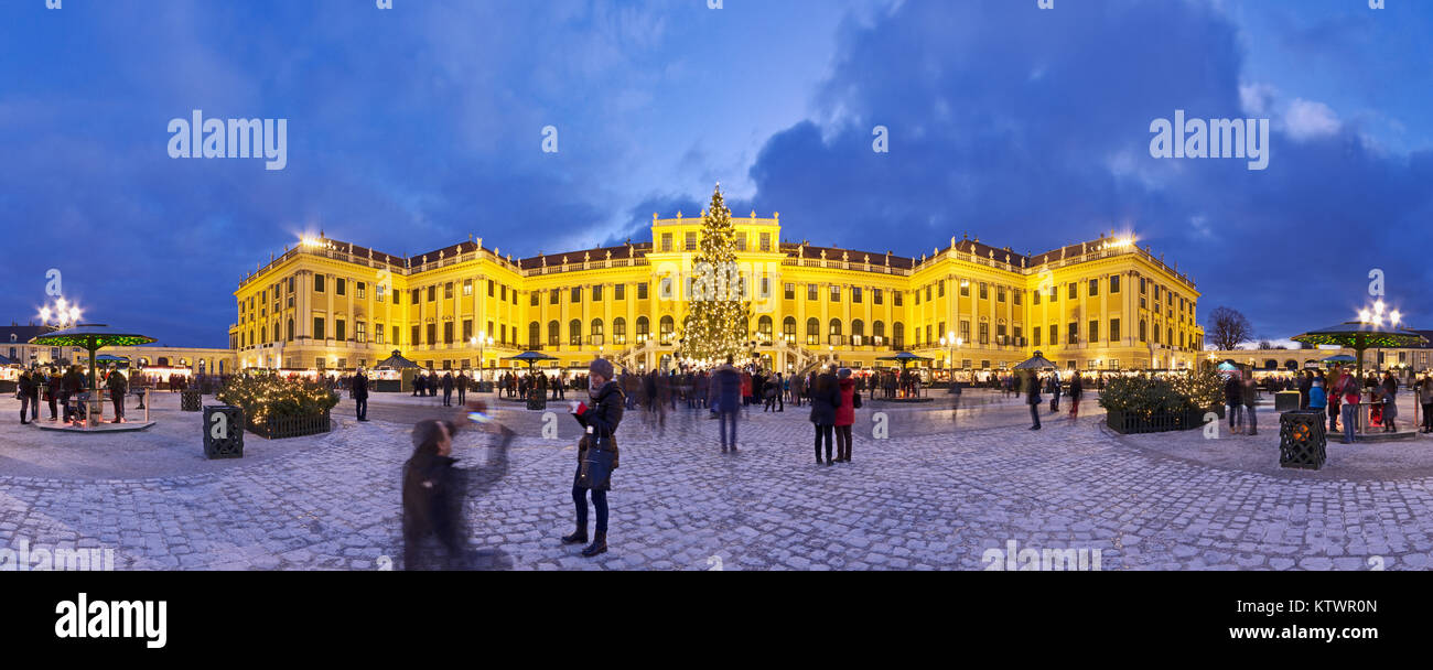Panormaic view of illuminated Schönbrunn palace in Christmas time with fairy lights decorated Christmas tree and market at blue hour dusk in Advent. Stock Photo