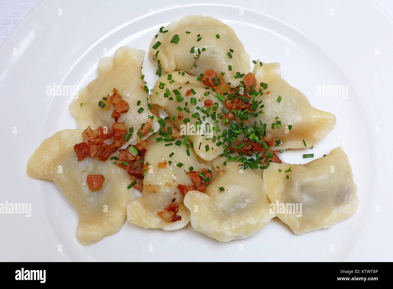 Plate of pierogi or varenyky stuffed filled dumplings with bacon crisps and green chive onion, traditional East Europe cuisine meal popular in Poland, Stock Photo